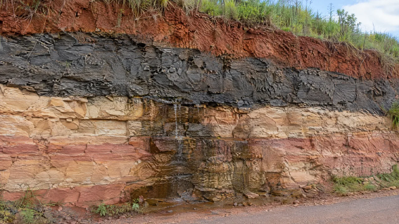 Corte de estrada com camadas de arenito e argila, o arranjo que forma um aquífero confinado